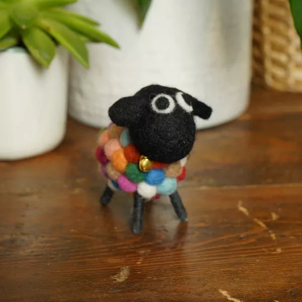 Small black sheep figurine with a colorful scarf on a wooden surface with plants in the background