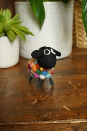 Small black sheep figurine with a colorful scarf on a wooden surface with plants in the background