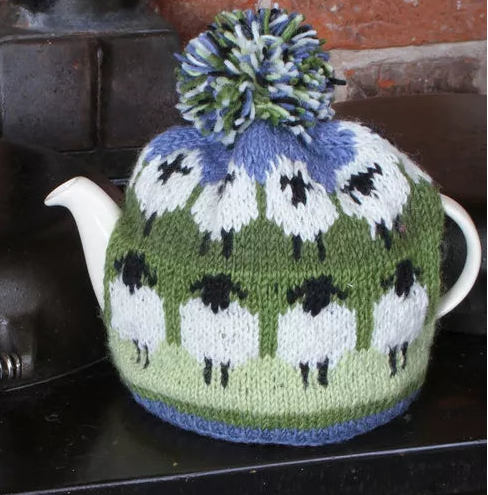 Knitted teapot cozy with sheep pattern on a stove