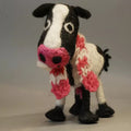 Knitted cow toy with a pink scarf on a plain background