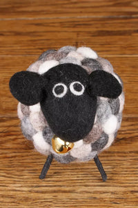 Felted sheep figurine with a bell on a wooden surface