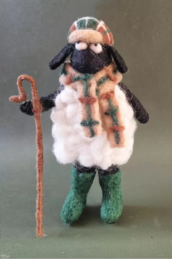 Felted sheep figurine with a checkered scarf, green boots, and a brown staff on a gray background