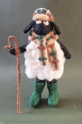 Felted sheep figurine with a checkered scarf, green boots, and a brown staff on a gray background