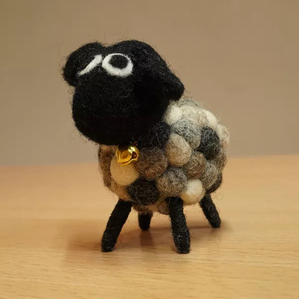 Small felted sheep figurine with a black face and multicolored wool on a wooden surface.
