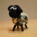 Small felted sheep figurine with a black face and multicolored wool on a wooden surface.