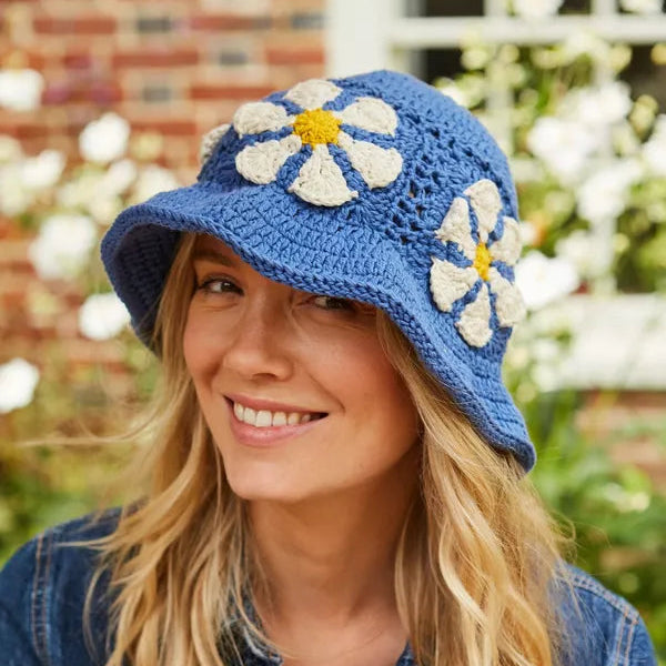 Woman wearing a blue crochet hat with floral decorations outdoors.