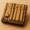 Wooden coaster with engraved design of a deer in a forest on a beige background