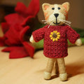 Small teddy bear toy wearing a red sweater with a yellow flower on a beige surface.