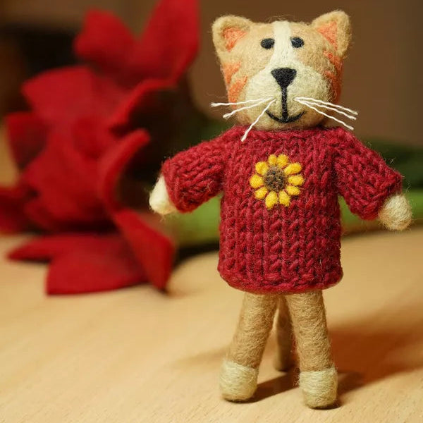 Small teddy bear toy wearing a red sweater with a yellow flower on a beige surface.