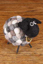 Felted sheep toy with a black face and gold tag on a wooden surface