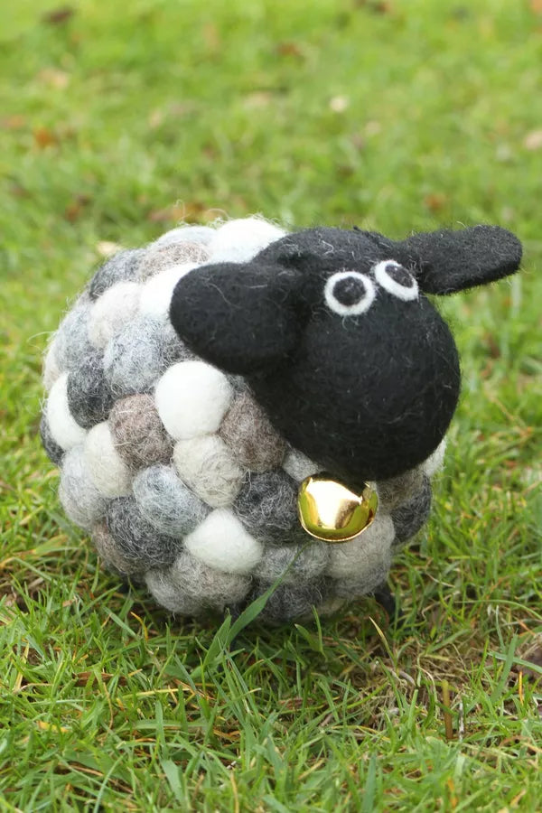 Sheep-shaped ball with a black face and gold bell on grass