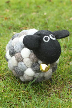 Sheep-shaped ball with a black face and gold bell on grass